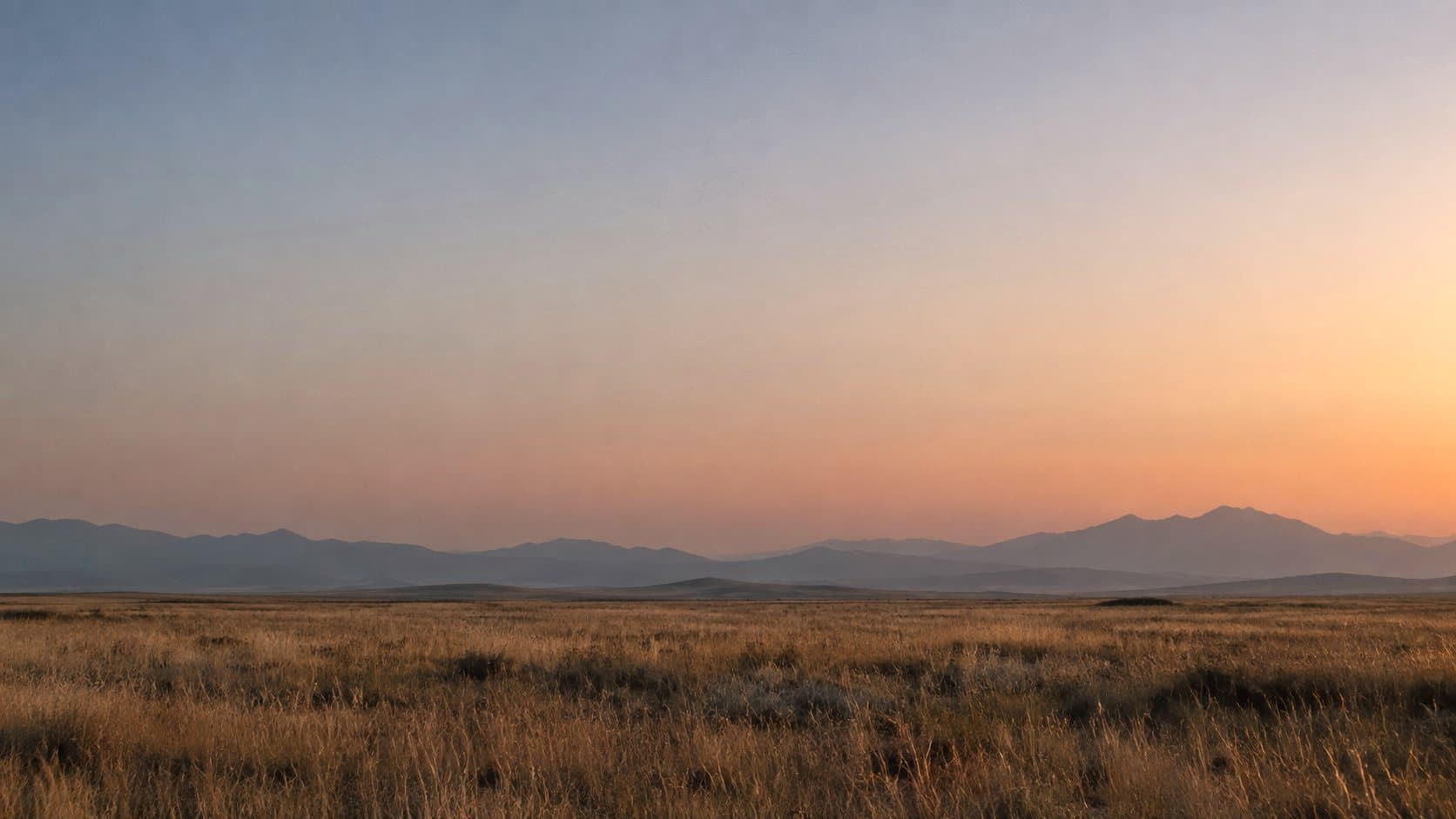 An open plain at dusk, with hazy mountains along the horizon