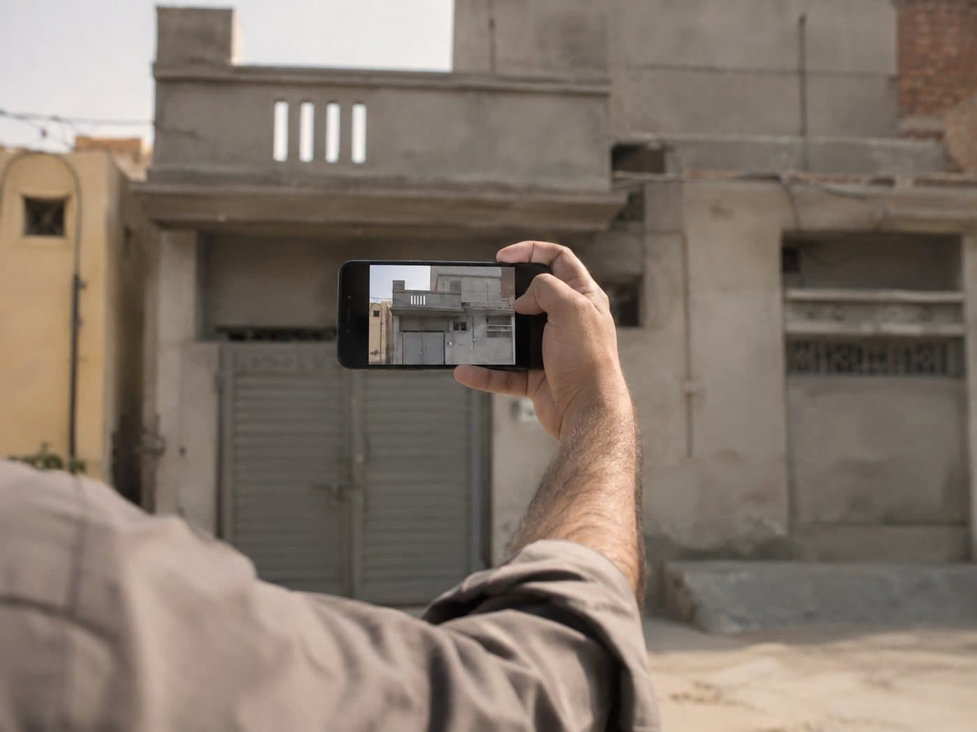 A man holding up a phone to photograph the front of his own house